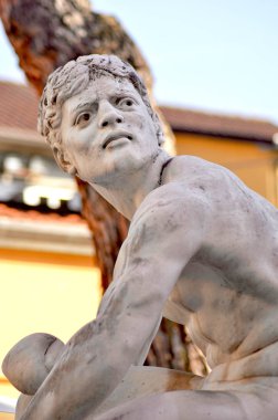 Klasik bir heykel oturan bir genç adam gösterilen beyaz mermerden. O bir yana, omzunun üzerinden arıyor. Bir ağaç ve bir binanın duvarına arka planda ve Gökyüzü mavidir.