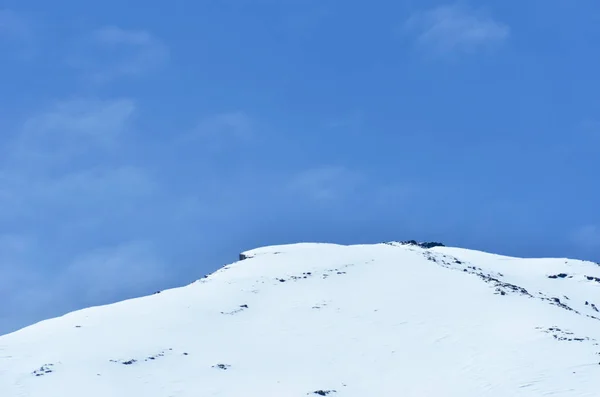 A hóború hegy szélén egy kék eget láttunk, néhány fehér felhőt. — Stock Fotó
