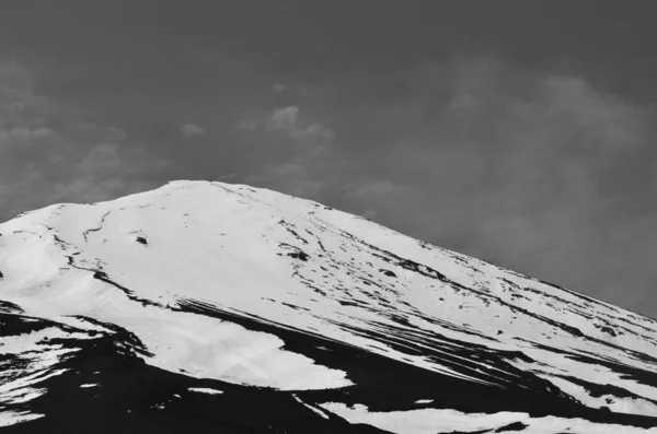 Uma imagem em preto e branco de uma cordilheira coberta de neve contra um céu nublado . — Fotografia de Stock