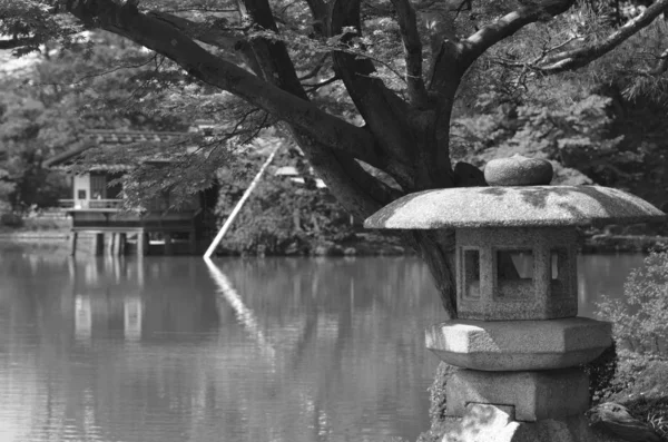 Una fotografía en blanco y negro de una linterna de piedra japonesa junto a un estanque . — Foto de Stock