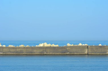 Mavi bir denize ve gökyüzüne karşı görülen üçgen beton karşı ağırlıklarla kaplı bir dalgakıran.