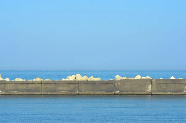 Um quebra-mar coberto de contrapesos de concreto triangular visto contra um mar e céu azuis . — Fotografia de Stock