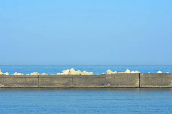 Eine mit dreieckigen Betongegengewichten bedeckte Buhne, die vor blauem Meer und Himmel steht. — Stockfoto