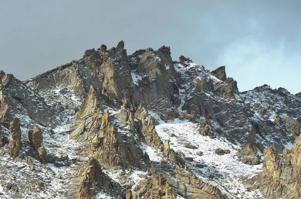 白雪覆盖的山顶上的岩石摇曳成阴的天空 下过雪了 这片土地荒芜 没有植被 — 图库照片