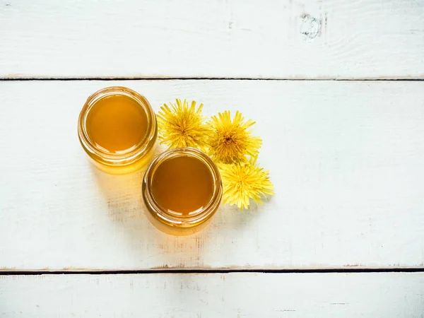 Yellow, bright dandelions, flower honey in a jars on a beautiful, white, wooden table. Top view, close-up. Concept of a tasty and healthy meal