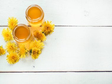 Sarı, parlak dandelions, güzel, beyaz, ahşap bir tablo üzerinde bir kavanoz bal çiçek. Üstten görünüm, yakın çekim. Bir lezzetli ve sağlıklı yemek kavramı