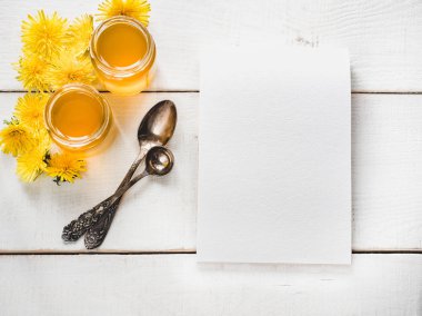 Parlak dandelions, defter, yazıtlar için boş bir sayfa ile bir kavanoz, güzel, beyaz, ahşap bir tablo üzerinde vintage kaşık bal çiçek. Üstten görünüm, yakın çekim. Bir lezzetli ve sağlıklı yemek kavramı