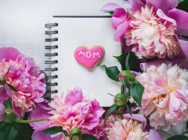 Parlak, pembe kalp kurabiye kelimesiyle Anne, çiçek açan şakayık çiçekleri arka plan üzerinde yazıtlar tebrik için boş bir sayfa ile bir sketchbook şeklinde. Üstten görünüm, yakın çekim, izole