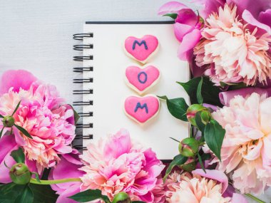 Parlak, pembe kalp kurabiye kelimesiyle Anne, çiçek açan şakayık çiçekleri arka plan üzerinde yazıtlar tebrik için boş bir sayfa ile bir sketchbook şeklinde. Üstten görünüm, yakın çekim, izole