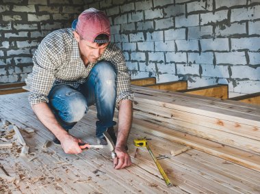 Ahşap inşaat altında evin içinde araçlarla çalışma şık adam bir beyzbol şapkası, kot pantolon ve tişört. İnşaat ve onarım kavramı