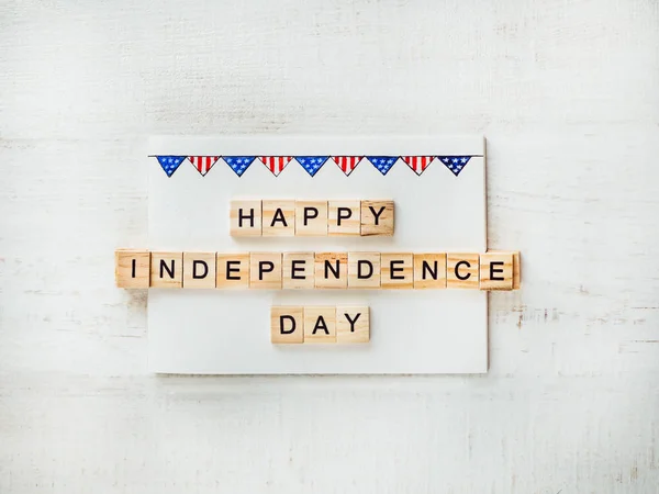 US flag and wooden letters of the alphabet with congratulations on the US Independence Day on a white background. Top view, close-up. Preparation for the Independence Day