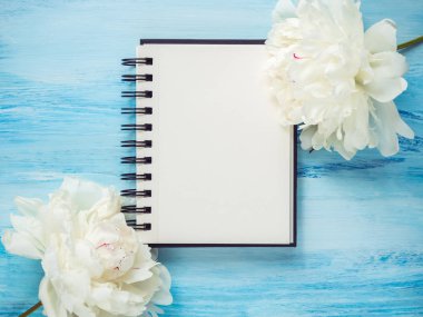 Beyaz çiçek açan, buket peonies ve bir boş Not Defteri sayfası notlarınızın hassas üzerinde mavi arka plan. Üstten görünüm, yakın çekim. Sevgi ve mutluluk kavramı. Düğün davetiyesi