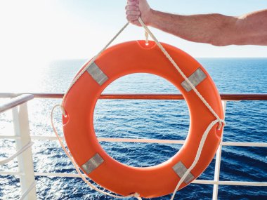 Parlak, turuncu lifebuoy cruise liner üst güvertede dalgalar deniz, sabah güneşi ve açık, mavi gökyüzü bir arka planda tutan erkek el. Güvenlik, bakım ve yardım kavramı