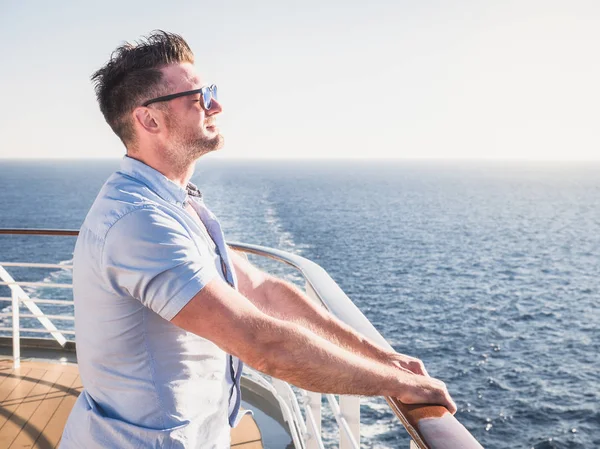Çekici erkek güneş gözlüğü mesafe bir gün batımı arka planı içine bakan gemisi üst güvertede. Deniz seyahat ve eğlence kavramı