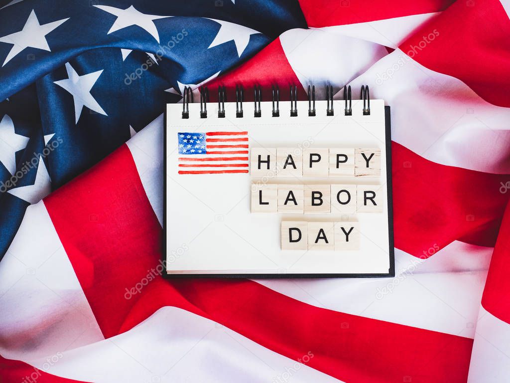 Notepad with blank page, wooden letters of the alphabet in the form of the words Labor Day on the background of the US Flag. Top view, close-up