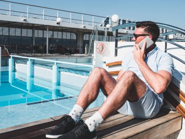 Bir cruise gemi havuzu ve mavi gökyüzü arka plan üzerinde bir açık güverte üzerinde telefonda konuşan adam gülümseyen