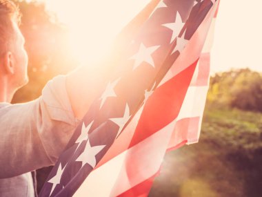 Çekici bir adam bir ABD bayrağı batan güneşin ışınları arka planı holding. Arkadan görüntüleyin. Tatil için hazırlanıyor