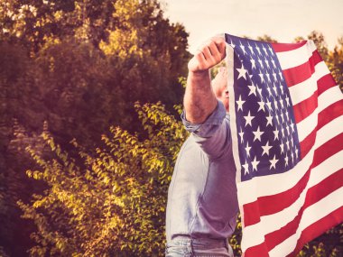 Rüzgar bize ayar güneş ışınlarının zemin karşı bayrak sallayarak tutan çekici bir adam. Arkadan, closeup görüntüleyin. Tatil için hazırlanıyor