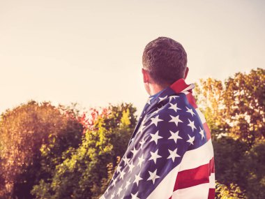 Rüzgar bize ayar güneş ışınlarının zemin karşı bayrak sallayarak tutan çekici bir adam. Arkadan, closeup görüntüleyin. Tatil için hazırlanıyor