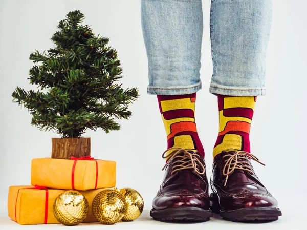 Men\'s legs, funny socks, stylish shoes, gifts with a red ribbon and a Christmas tree. White background, isolated, close-up. Preparing for the holidays