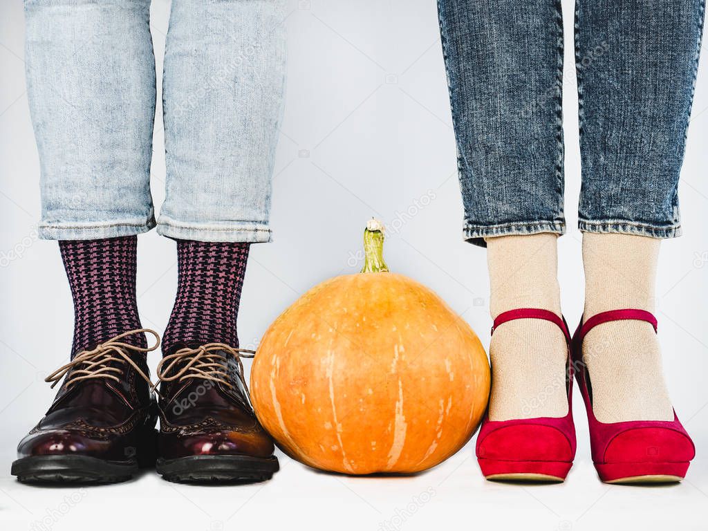 Ripe pumpkins, legs of a young couple in stylish shoes, bright, colorful socks. White background, isolated, close-up. Holidays, fashion, elegance