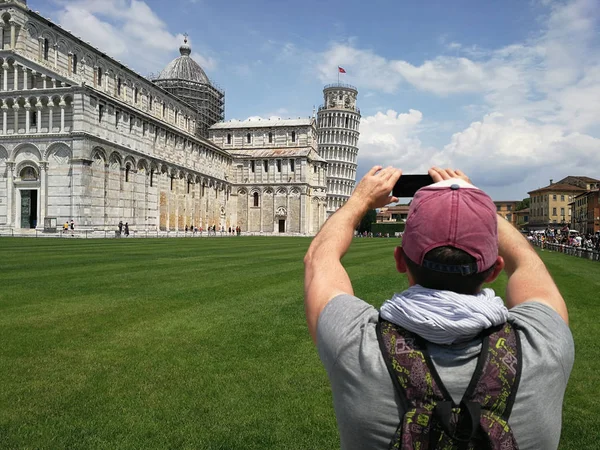 Stylish guy with a phone taking pictures of the Leaning Tower of Pisa on a sunny, clear day. Concept of recreation, travel and tourism