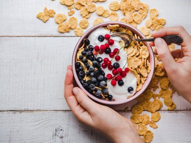 Sağlıklı kahvaltı el, Mısır gevreği, yoğurt ve bir beyaz tahta arka plan üzerinde taze çilek ile top. Portre, üstten görünüm, izole. Sağlıklı ve lezzetli yiyecek kavramı