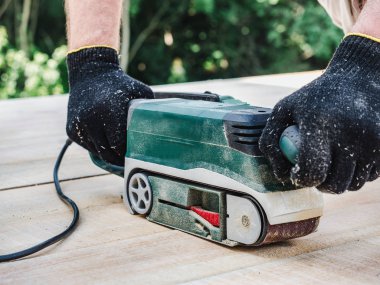 Güçlü erkekler ellerini ve ahşap ile yeşil ağaçlar arka plan üzerinde çalışmak için bir makine. Yakın çekim yan görünüm. İnşaat ve onarım kavramı