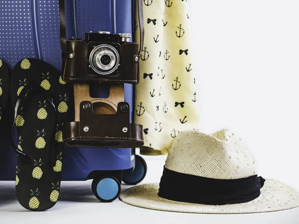 Stylish, blue suitcase, vintage camera and sun hat on a white, isolated background. Close-up. Preparing for the summer trip
