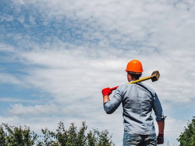Parkta yeşil ağaçların arka planında elinde balyoz tutan çekici bir adam. Yakın plan. Çalışma ve istihdam kavramı