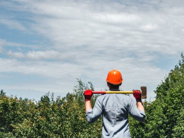Parkta yeşil ağaçların arka planında elinde balyoz tutan çekici bir adam. Yakın plan. Çalışma ve istihdam kavramı