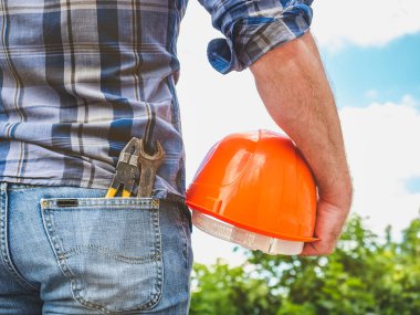 Güvenlik kaskı tutan aletleri olan yakışıklı bir adam. Arkadan bak, yakın plan. İş ve istihdam kavramı