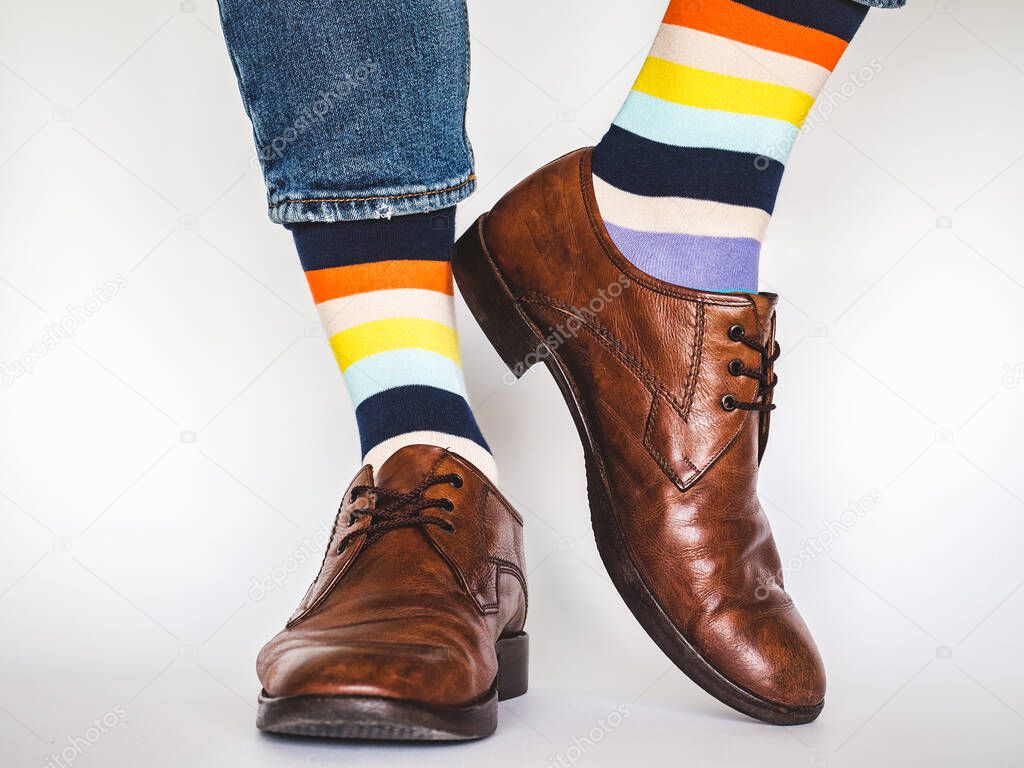 Men's legs, trendy shoes, blue jeans and variegated, long socks on a white, isolated background. Close-up. Concept of style and elegance