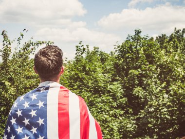 Açık ve güneşli bir günde mavi arka planda Amerikan Bayrağı tutan çekici bir adam. Arkadan bak, yakın plan. Ulusal tatil konsepti