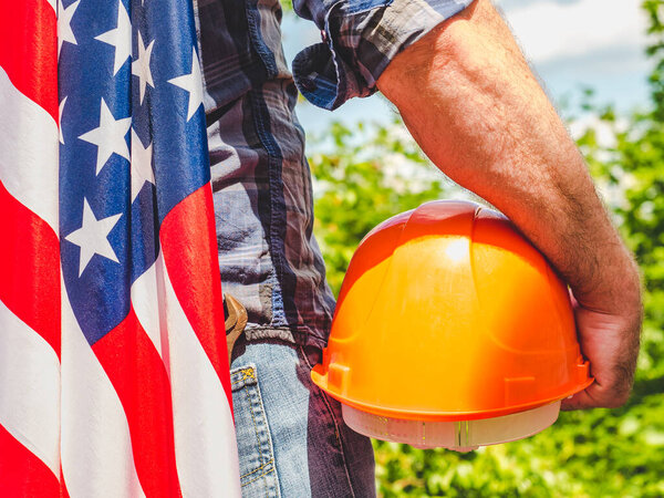 Handsome man with tools, holding an American Flag. View from the back, close-up. Concept of work and employment