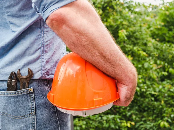 Attractive man with tools, holding a safety helmet. View from the back, close-up. Concept of work and employment