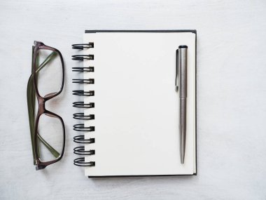 Boş not defteri sayfası, kalem ve gözlük. Tebrik kartı. Yakın çekim, yukarıdan manzara, ahşap yüzey. Profesyonel bir tatil için hazırlık kavramı. Akrabalar, arkadaşlar ve meslektaşlar için tebrikler.