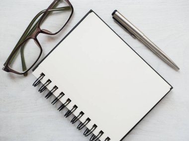 Boş not defteri sayfası, kalem ve gözlük. Tebrik kartı. Yakın çekim, yukarıdan manzara, ahşap yüzey. Profesyonel bir tatil için hazırlık kavramı. Akrabalar, arkadaşlar ve meslektaşlar için tebrikler.