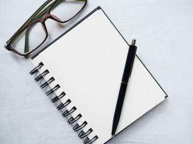 Boş not defteri sayfası, kalem ve gözlük. Tebrik kartı. Yakın çekim, yukarıdan manzara, ahşap yüzey. Profesyonel bir tatil için hazırlık kavramı. Akrabalar, arkadaşlar ve meslektaşlar için tebrikler.
