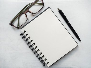 Boş not defteri sayfası, kalem ve gözlük. Tebrik kartı. Yakın çekim, yukarıdan manzara, ahşap yüzey. Profesyonel bir tatil için hazırlık kavramı. Akrabalar, arkadaşlar ve meslektaşlar için tebrikler.