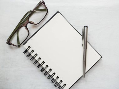 Boş not defteri sayfası, kalem ve gözlük. Tebrik kartı. Yakın çekim, yukarıdan manzara, ahşap yüzey. Profesyonel bir tatil için hazırlık kavramı. Akrabalar, arkadaşlar ve meslektaşlar için tebrikler.