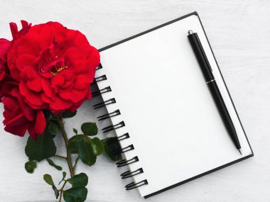 Boş bir not defteri ve güzel bir çiçek. Yakın çekim, yukarıdan manzara, ahşap yüzey. Profesyonel bir tatil için hazırlık kavramı. Akrabalar, arkadaşlar ve meslektaşlar için tebrikler.