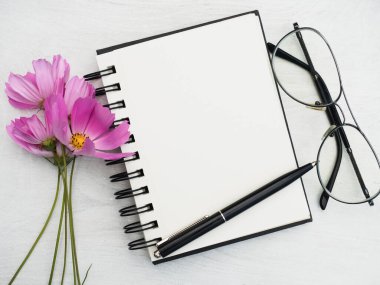 Boş bir not defteri ve güzel bir çiçek. Yakın çekim, yukarıdan manzara, ahşap yüzey. Profesyonel bir tatil için hazırlık kavramı. Akrabalar, arkadaşlar ve meslektaşlar için tebrikler.