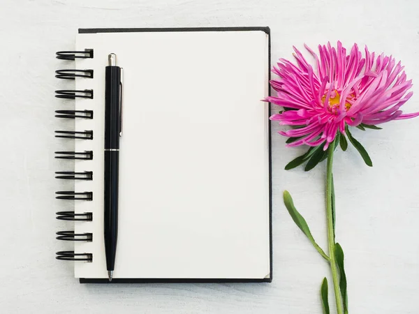 Boş bir not defteri ve güzel bir çiçek. Yakın çekim, yukarıdan manzara, ahşap yüzey. Profesyonel bir tatil için hazırlık kavramı. Akrabalar, arkadaşlar ve meslektaşlar için tebrikler.