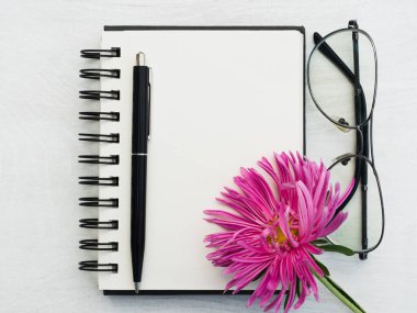 Boş bir not defteri ve güzel bir çiçek. Yakın çekim, yukarıdan manzara, ahşap yüzey. Profesyonel bir tatil için hazırlık kavramı. Akrabalar, arkadaşlar ve meslektaşlar için tebrikler.