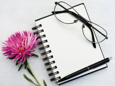 Boş bir not defteri ve güzel bir çiçek. Yakın çekim, yukarıdan manzara, ahşap yüzey. Profesyonel bir tatil için hazırlık kavramı. Akrabalar, arkadaşlar ve meslektaşlar için tebrikler.