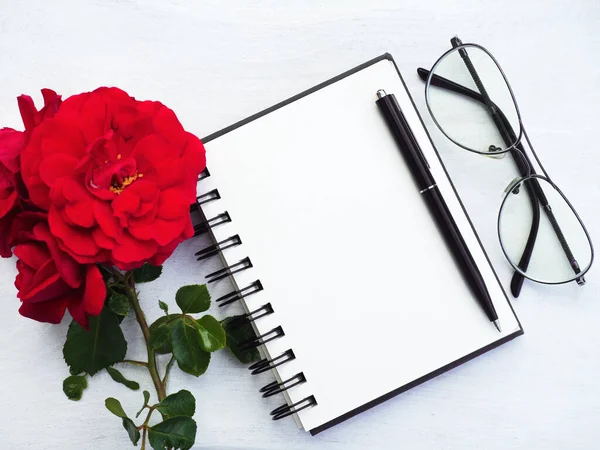 Blank notepad page and a beautiful flower. Close-up, view from above, wooden surface. Concept of preparation for a professional holiday. Congratulations for relatives, friends and colleagues