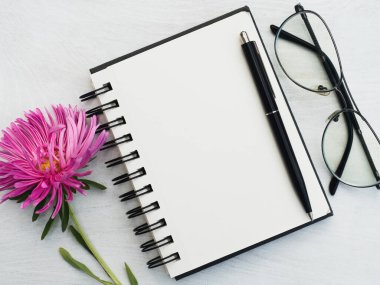 Boş bir not defteri ve güzel bir çiçek. Yakın çekim, yukarıdan manzara, ahşap yüzey. Profesyonel bir tatil için hazırlık kavramı. Akrabalar, arkadaşlar ve meslektaşlar için tebrikler.