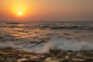 Bir yaz akşamı gün batımında kayalara çarpan dalgaların görüntüsünü izleyin. İsrail, Ashkelonf. Bir yaz akşamı gün batımında kayalara çarpan dalgalar.