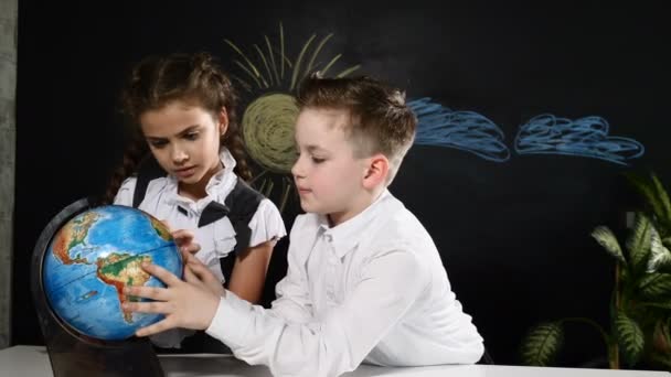 Concept van de school. Schoolkinderen zitten aan een bureau met een wereldbol. Kinderen kiezen een plek om te reizen op vakantie — Stockvideo